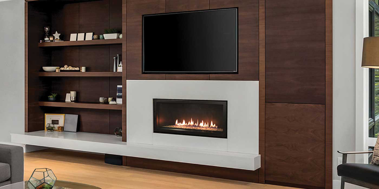 The Empire Contemporary Boulevard Direct Vent Gas Fireplace installed into an entertainment center in a living room with brown shelves and a large TV mounted over the fireplace.