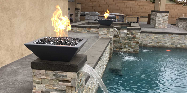 An outdoor pool with fire and water bowls installed on the side