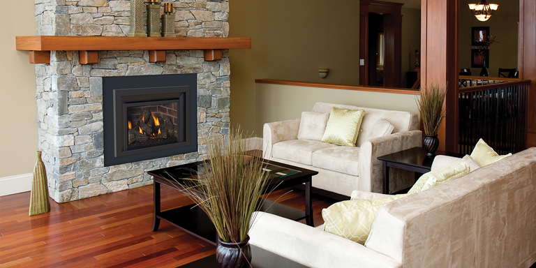A traditional living space with two couches, a natural stone hearth with a wooden mantel, and a wood burning stove insert from Ironstrike