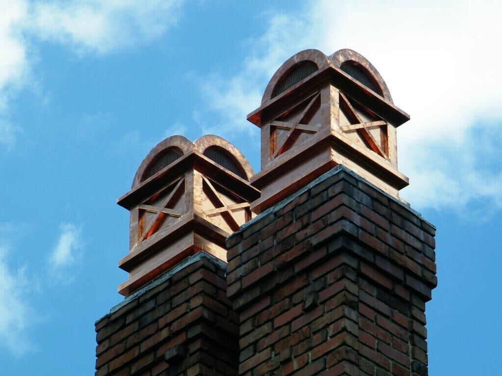 A close-up view of a traditional, masonry chimney with two openings and two decorative, copper chimney caps.