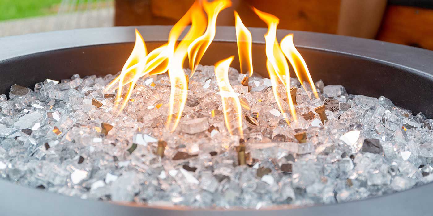 A close-up view of a concrete gas fire bowl with clear, reflective fire glass media.