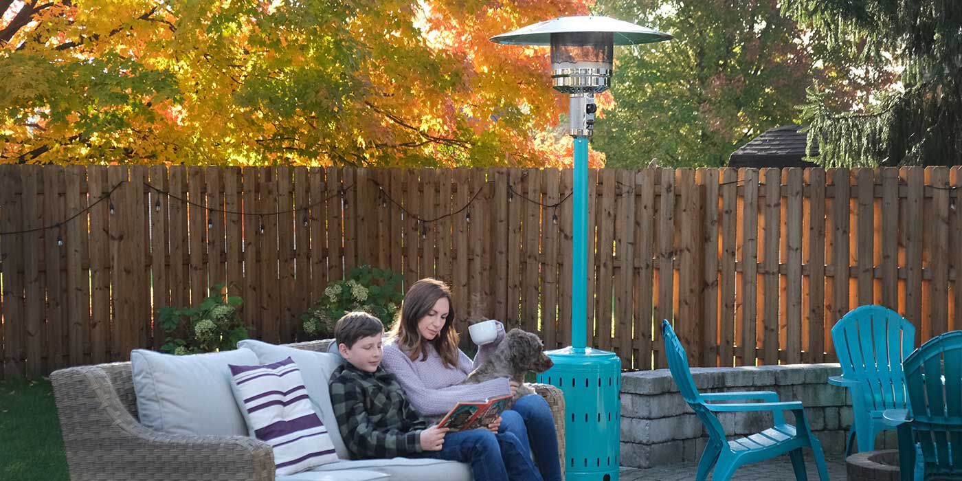 An outdoor patio space in the fall with a mother and son reading a book on the sofa and an aqua-colored Propane patio heater nearby