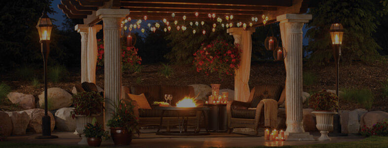 An outdoor patio space under a decorative white gazebo with fairy lights in the rafters, a lounge furniture set, and a gas fire table.