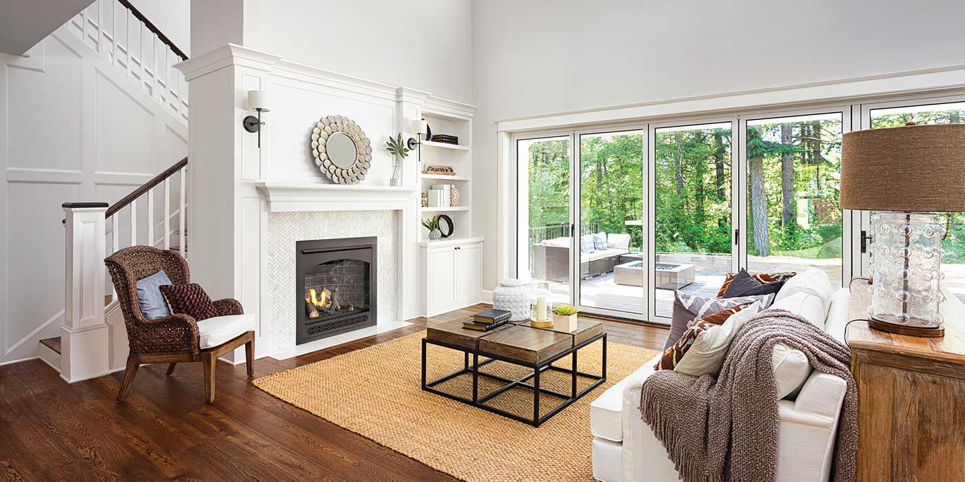 A see-through gas fireplace installed on a white wall in contemporary-style living room with a white couch, a yellow accent chair, and light wood furniture.