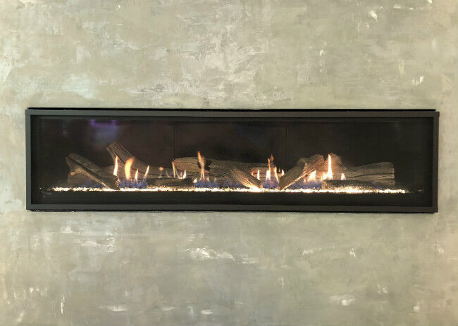 Black linear fireplace with glowing fire, crystal fire glass, and driftwood logs in a cement hearth
