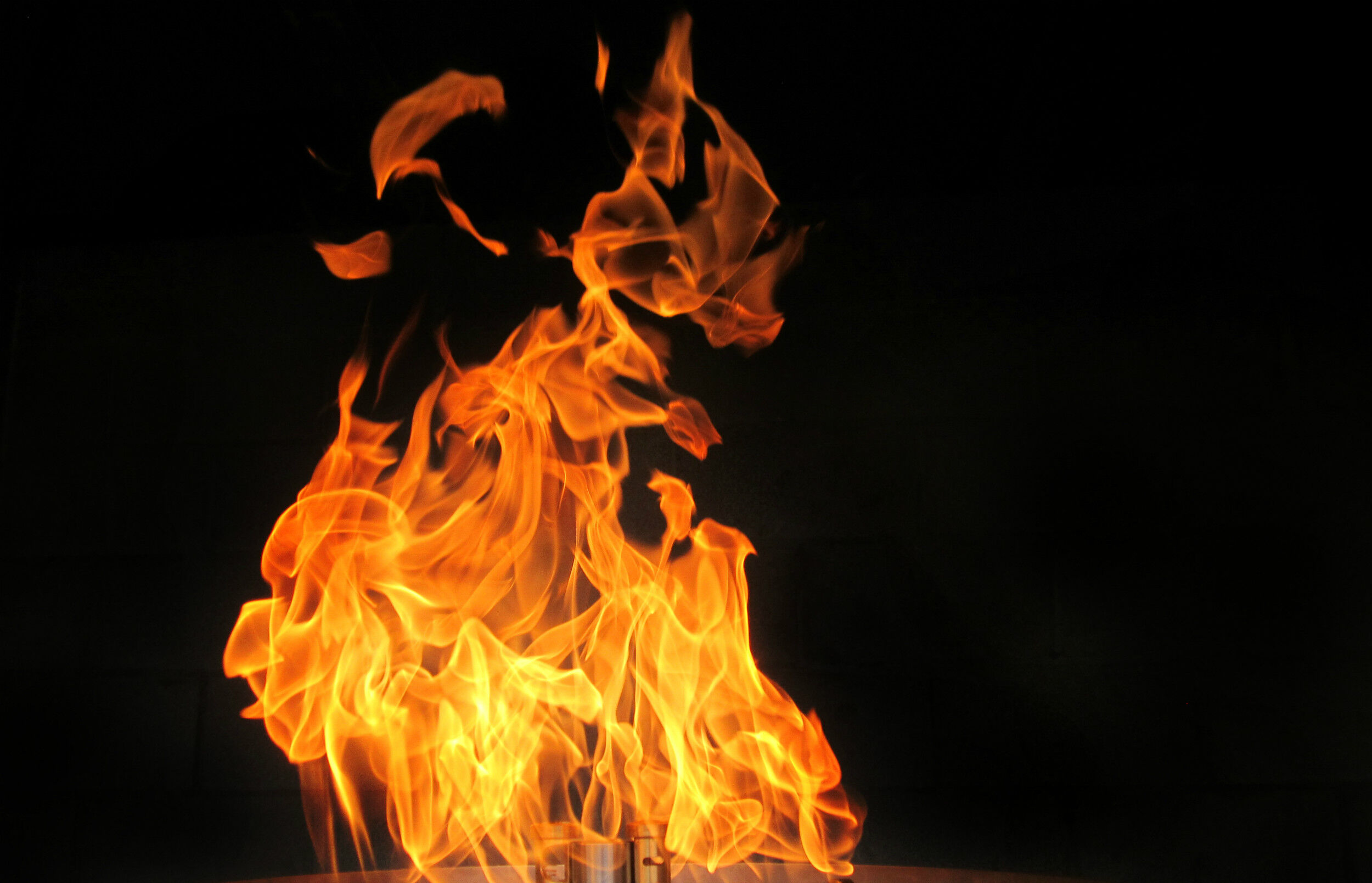 A close-up view of a tall, robust, orange and yellow flame on a solid black background.