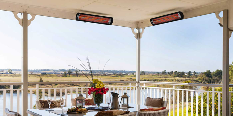 An outdoor patio space with a large dining table and chairs and two Bromic Tungsten patio heaters mounted to the ceiling
