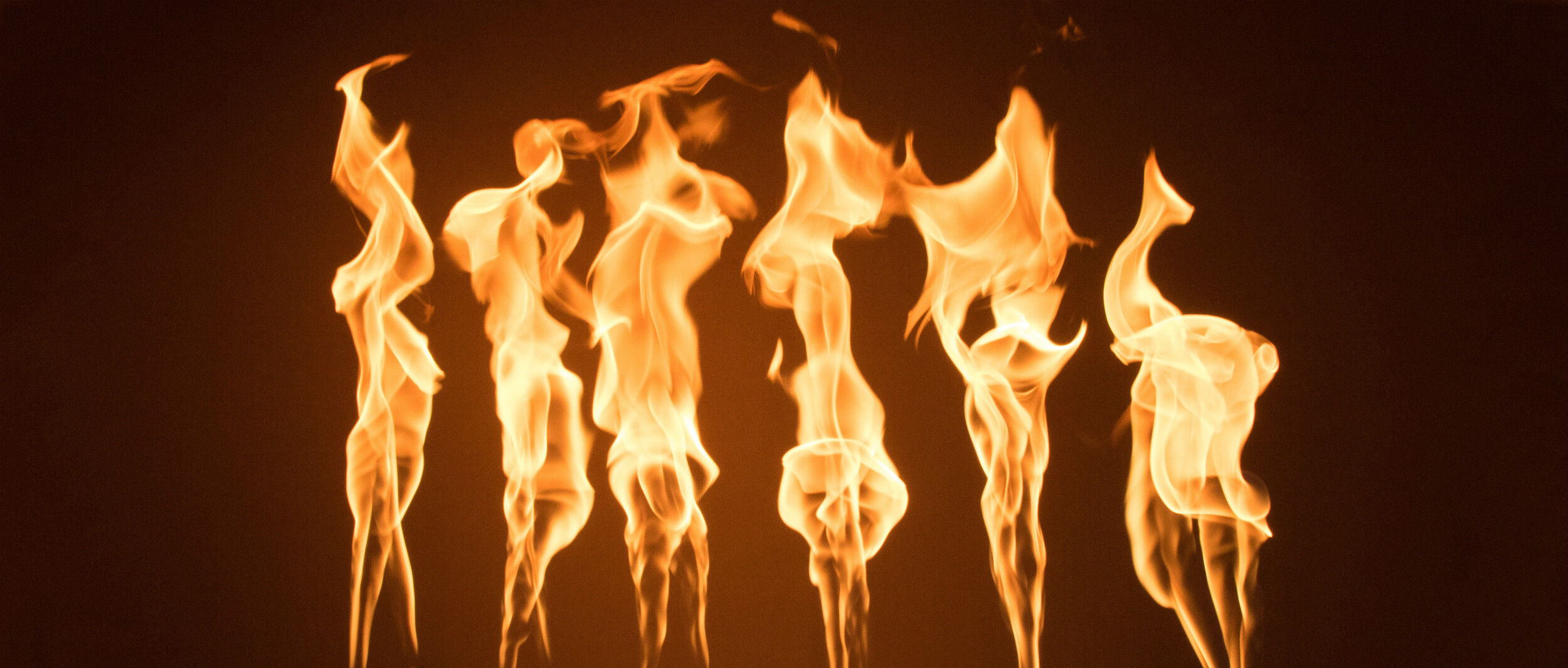 A close-up view of individual, tall orange flames coming out of a gas fire pit burner.