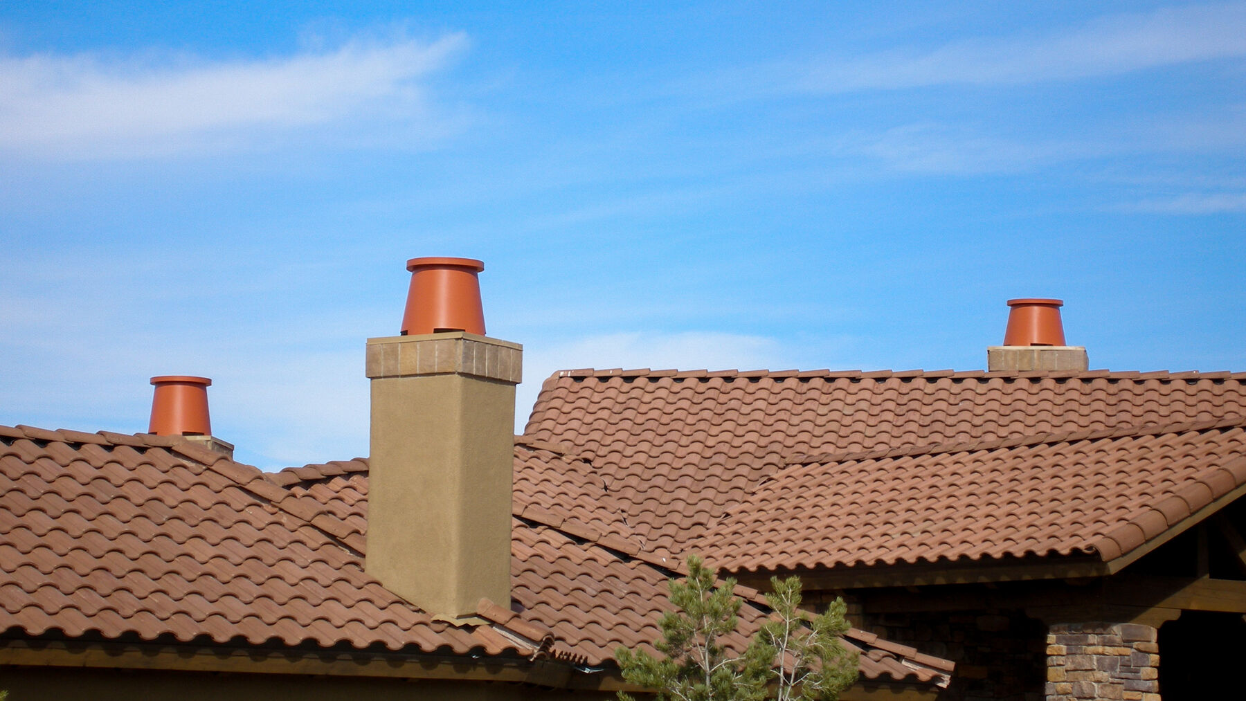 A rooftop finished with brown roof tiles that has three chimney stacks with brown clay chimney pots.