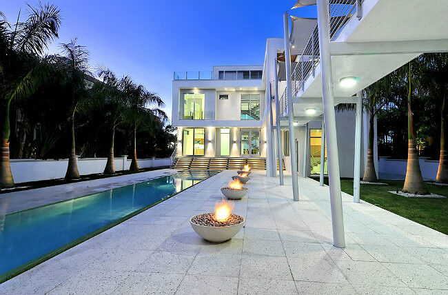 Stone patio with five gas fire bowls next to a swimming pool at an ultramodern luxury home