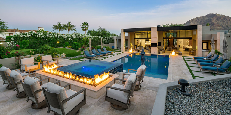 A luxurious outdoor space with a large pool and sitting area with a large, linear custom gas fire pit . 