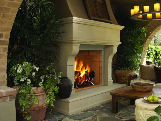 Superior's Outdoor Wood Burning Fireplace installed with a traditional-looking, white hearth, a brick firebox, and a large smoke dome, surrounded by potted plants and flowers.