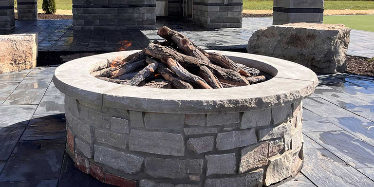 A custom-built masonry outdoor gas fire pit with a stack of rustic outdoor gas logs