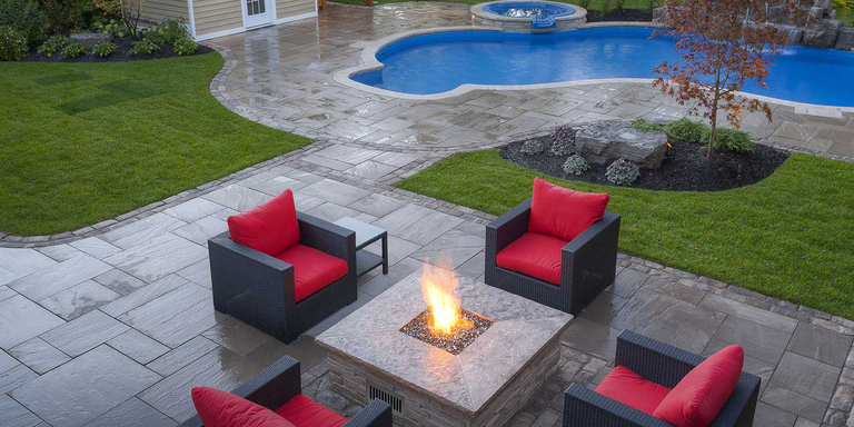 A large backyard that includes a sitting area with four red chairs and a gas fire pit, a shed, and an inground swimming pool