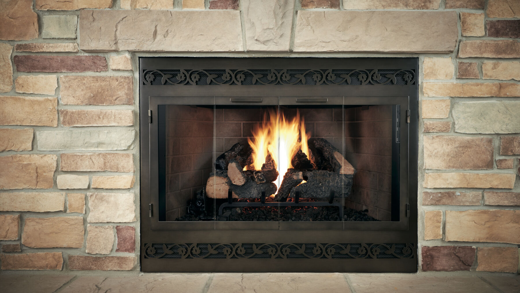 A traditional masonry hearth with a black fireplace, a log set, and distressed, bronze-colored tri-fold glass doors.