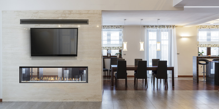 A linear see-through gas fireplace separating a modern indoor living room and a dining room