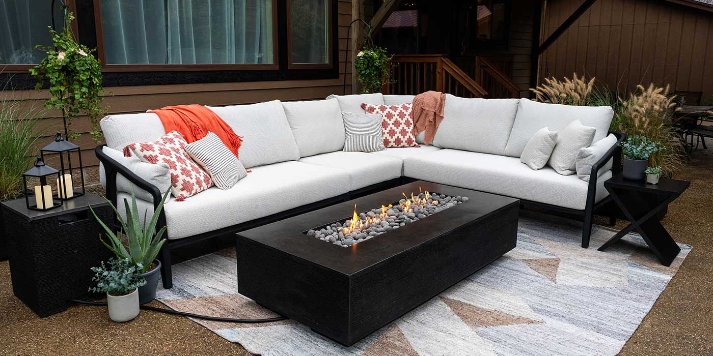An outdoor patio space with a lounge chair and a large stucco and stone gas fire pit with smooth black fire stones.