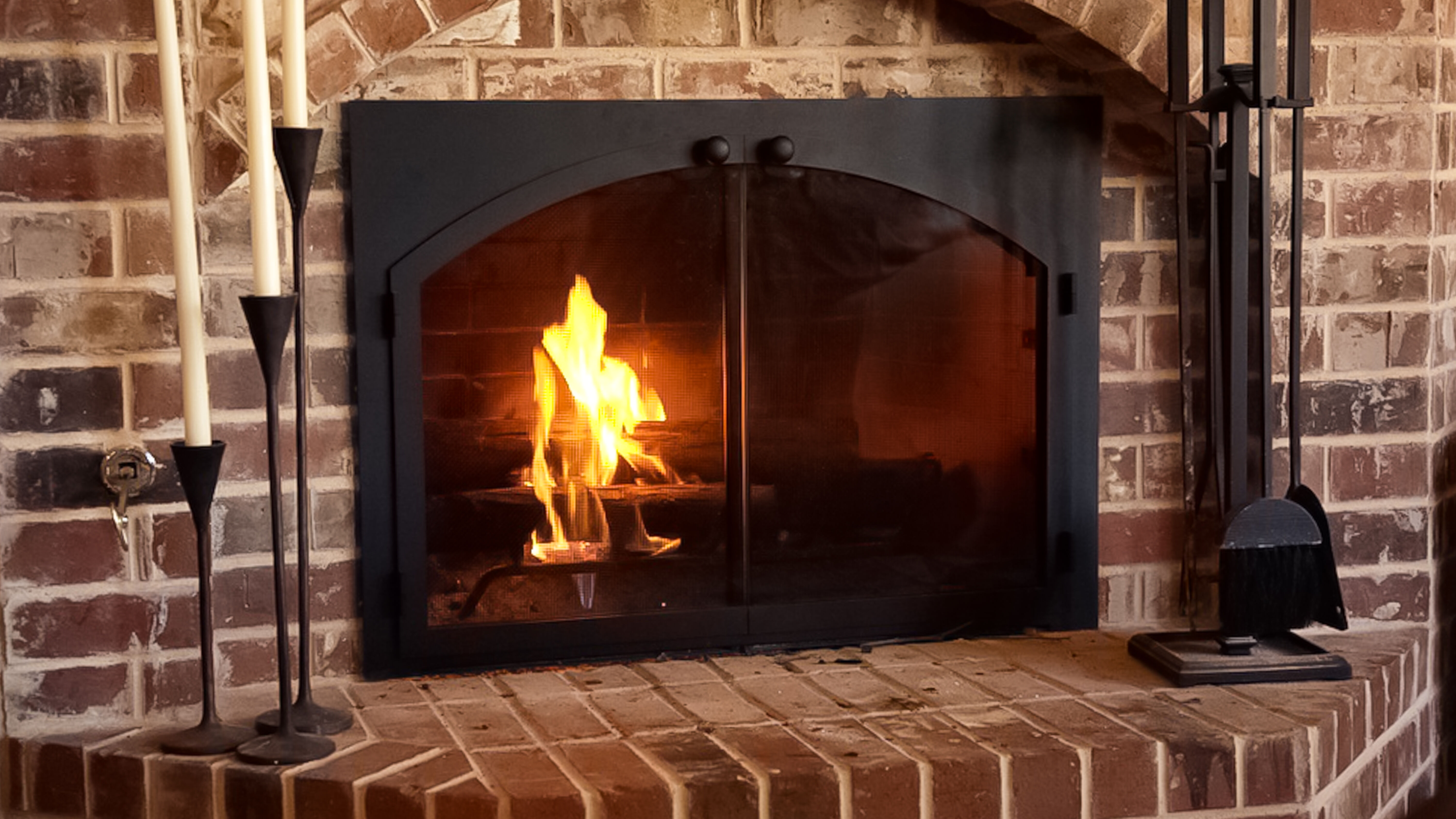 A traditional masonry hearth with a wood burning fireplace, black cast iron fireplace doors, and black fireplace tools.
