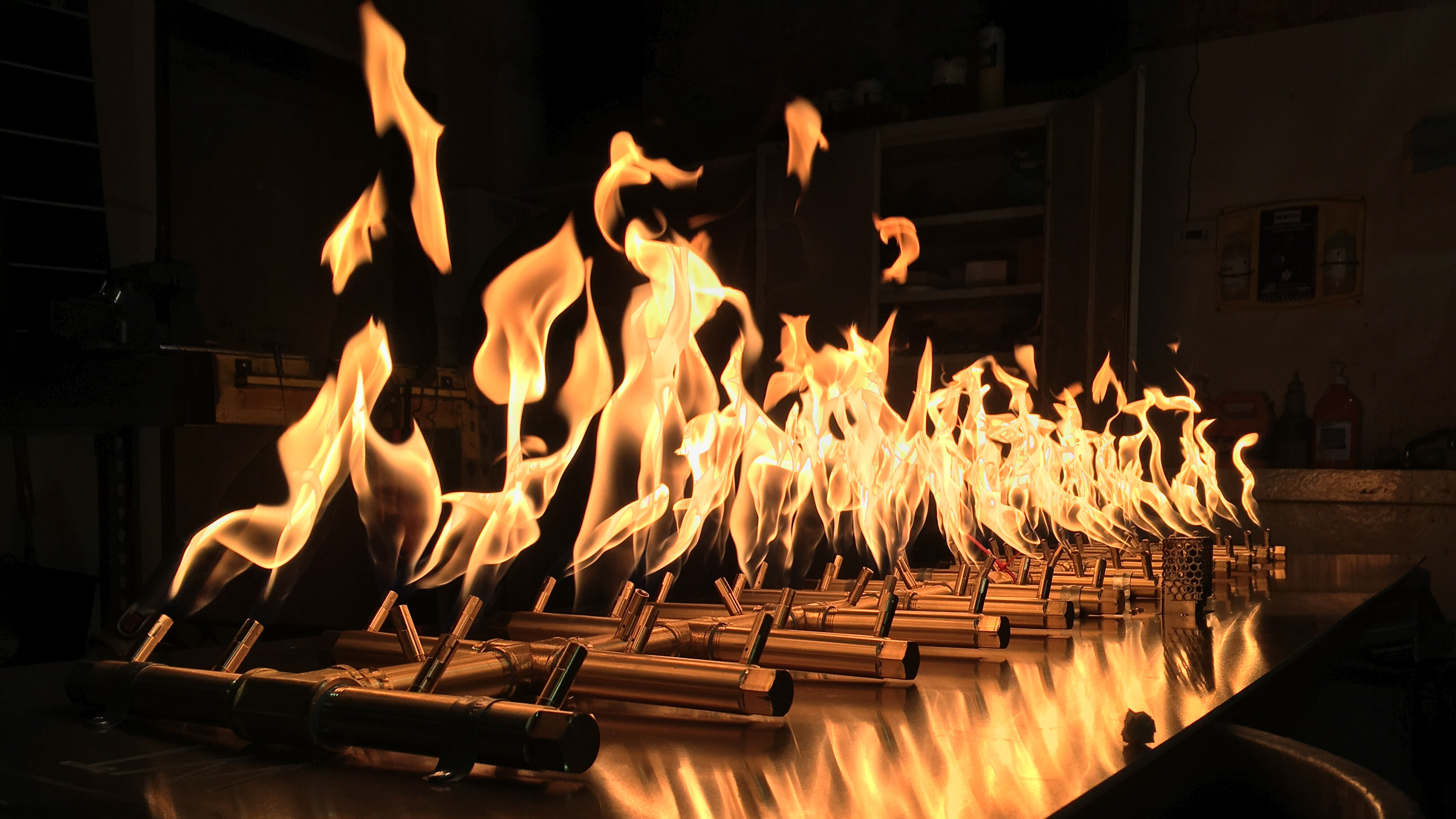 A close-up view of a brass tree-shaped gas fire pit burner with tall, orange flames.