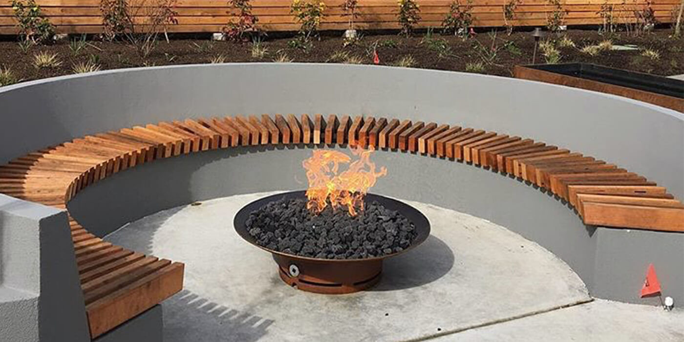 A custom-built fire pit area with a built-in seating wall surrounding a shallow metal gas fire bowl