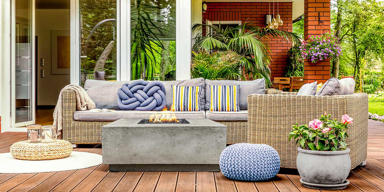 A natural, boho-inspired outdoor space with a Tavola 2 Gas Fire Pit from Prism Hardscapes, an outdoor sofa, and an outdoor chair