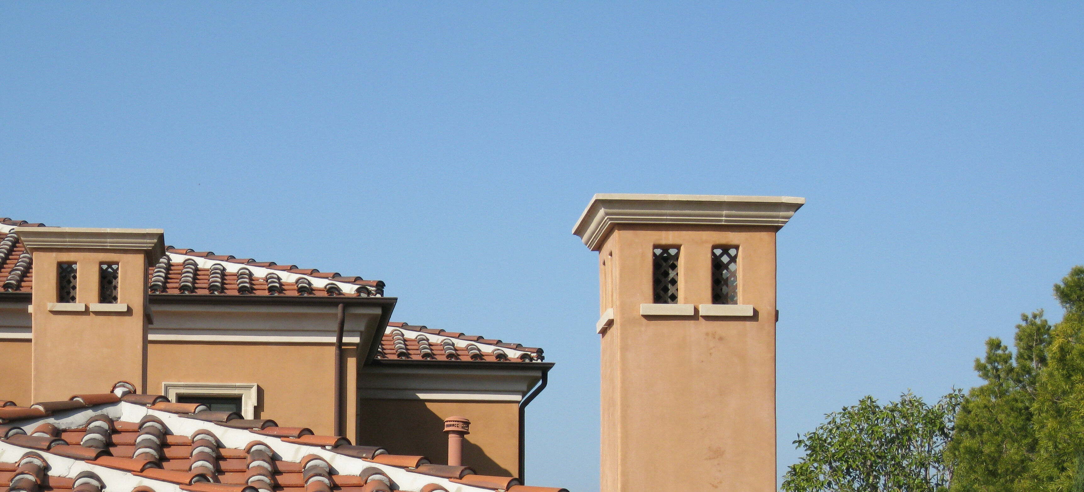 A rooftop with decorative brown roof tiles and two chimney stacks topped with chimney caps.