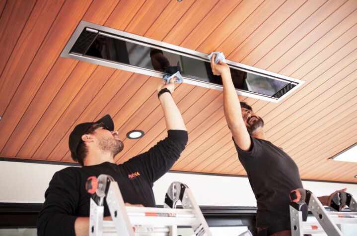 Two installers mounting a patio heater to the ceiling