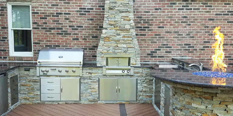 A large outdoor kitchen island with a grill, oven, storage doors, a bar area with seating, and a fire pit