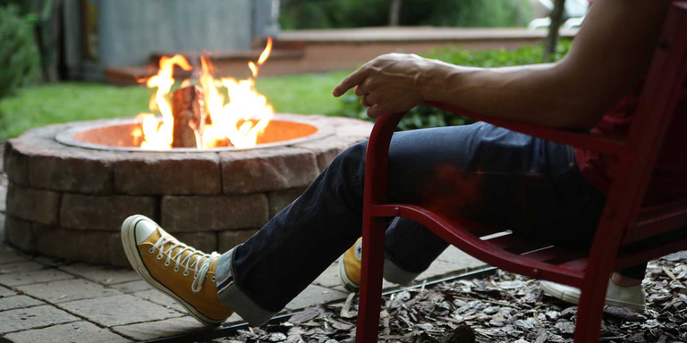 A person sitting next to a wood burning fire in the backyard.