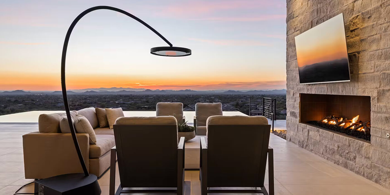 A contemporary outdoor lounging space with a linear electric fireplace and a Bromic Eclipse freestanding electric patio heater