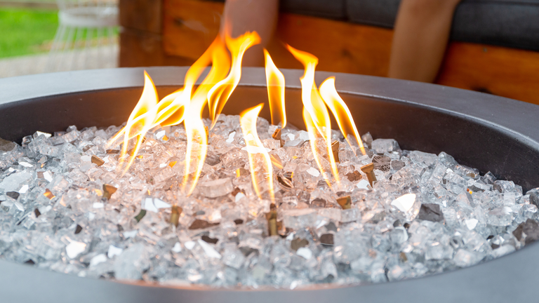 A close-up view of a white, 36-inch Tondo gas fire pit from FlameCraft with black lava rock media and an HPC gas fire pit burner.