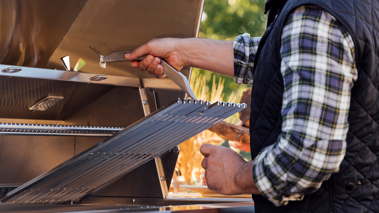 A man lifting up the grate on a stainless steel grill