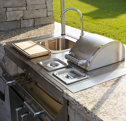 An outdoor kitchen with a stainless steel sink and faucet 